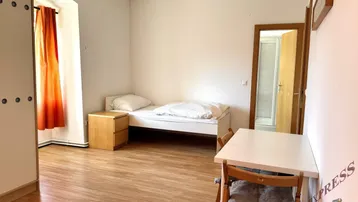 Helles Schlafzimmer mit Einzelbett, Schrank, Schreibtisch und Holzboden.