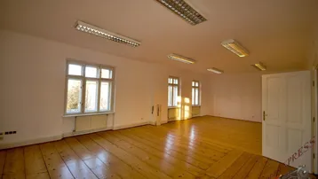 Geräumiger, heller Raum mit Dielenboden, mehreren Fenstern und weiß gestrichenen Wänden.