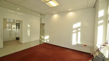 Helles Bürozimmer mit rotem Teppichboden, weißen Wänden und einer modernen Glasabtrennung zu einem weiteren Raum.