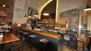 Gemütliche Bar mit langer Theke, Hockern und Tischen, beleuchtet von Pendelleuchten und indirektem Licht.
