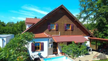 Vorderansicht des Hauses mit kleinem Pool, Holzfassade und braunem Ziegeldach unter blauem Himmel.