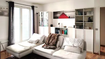 Helles Wohnzimmer mit bequemer Couch, weißen Schränken und Zugang zu einem französischen Balkon.