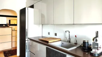 Moderne Küche mit glänzenden weißen Schränken, Spüle und Kaffeemaschine, offen zum Flur.