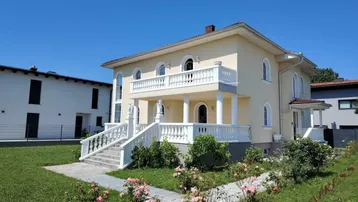 Elegante Villa mit klassischer Architektur, Balkon und gepflegtem Vorgarten unter blauem Himmel.
