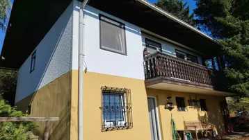 Fassade eines Hauses mit gelb-weißer Farbgebung und einem Holzbalkon im oberen Stockwerk.