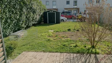 Gartenbereich mit Holzterrasse, Rasenfläche und Gartenhaus hinter dem Reihenhaus.