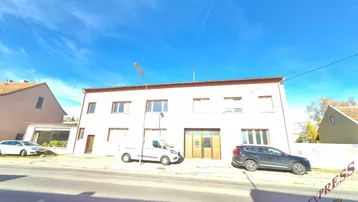 Gebäudeansicht von der Straße mit geparkten Fahrzeugen unter blauem Himmel.