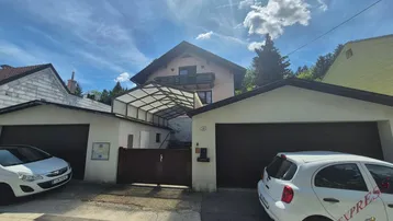 Vorderansicht des Hauses mit zwei Garagen und einer überdachten Zufahrt unter blauem Himmel.