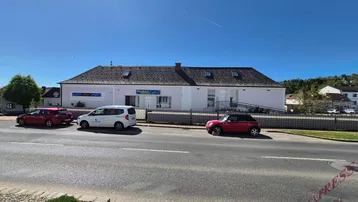 Ansicht des Gebäudes von der Straße mit parkenden Autos und klarem blauen Himmel.