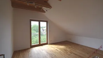 Helles Dachzimmer mit Holzbalken, Holzboden und Zugang zu einem französischen Balkon mit Blick ins Grüne.