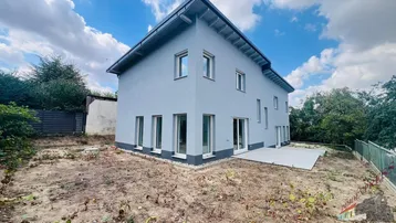 Neubau-Einfamilienhaus mit moderner grauer Fassade, großen Fenstern und einer vorbereiteten Terrasse.