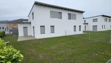 Rückseite eines modernen Reihenhauses mit großem Rasenbereich und Hecke.