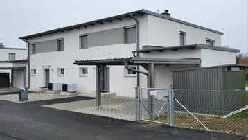 Moderne Doppelhaushälfte mit Carport und gepflastertem Vorplatz in einer Neubausiedlung.