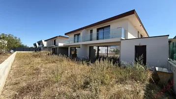 Moderne Neubau-Doppelhaushälfte mit Balkon und unfertigem Gartenbereich unter blauem Himmel.