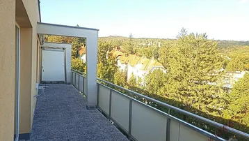 Langer Balkon mit Fliesenboden und weitem Blick ins Grüne und auf umliegende Gebäude.