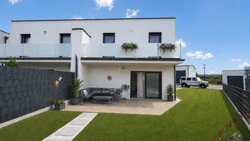 Moderne Reihenhausfassade mit privater Terrasse, kleinem Rasen und Balkon im Obergeschoss.