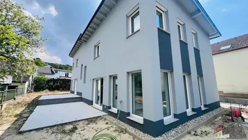 Modernes Einfamilienhaus mit grauer Fassade, großen Fenstern und einer neuen Terrasse im Rohbauzustand.