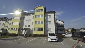 Mehrfamilienhaus mit hellgrüner Fassade und Außenparkplätzen unter blauem Himmel.