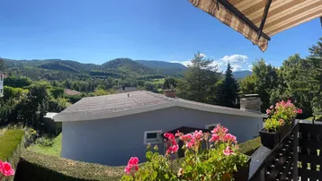 Panoramablick vom Balkon auf die weite, grüne Hügellandschaft unter blauem Himmel.