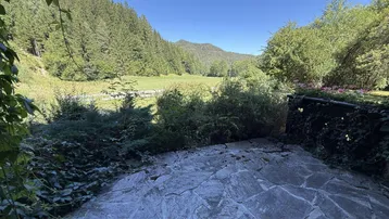 Weitläufiger Blick von der Steinterrasse über grüne Wiesen und bewaldete Hügel.