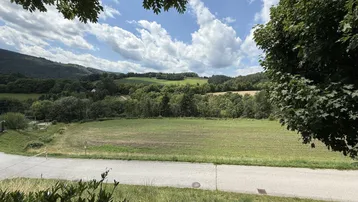 Weitläufiger Blick über grüne Felder und bewaldete Hügel unter blauem Himmel.