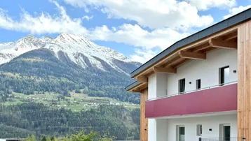 Modernes Gebäude mit Holzfassade und Balkonen, eingebettet in eine beeindruckende Berglandschaft.