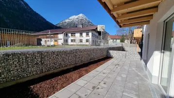 Gepflasterte Terrasse mit Gabionenmauer, Holzdachüberstand und beeindruckendem Bergblick.