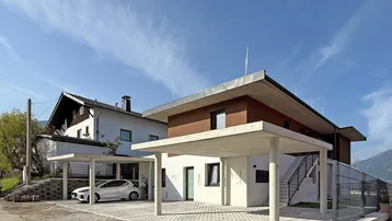 Modernes Wohnhaus mit zwei Carports und gepflasterter Einfahrt unter blauem Himmel.
