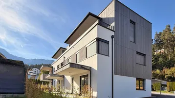 Moderne Architektur des Neubaus mit Holzverkleidung, Balkonen und Bergblick unter blauem Himmel.