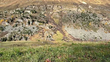 Berglandschaft mit grünen Hängen und felsigen Abhängen unter einem klaren blauen Himmel.