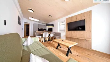 Modernes Wohnzimmer mit Holzboden, gemütlichem Sofa und integrierter Küche in offener Gestaltung.