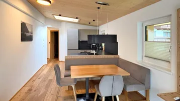 Heller Essbereich mit Holztisch und Sitzbank, angrenzend an die moderne Küche mit Fensterblick.