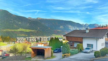 Weitläufiger Blick auf die umliegende Berglandschaft und benachbarte Häuser unter blauem Himmel.