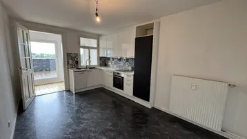 Moderne Küche mit weißen Schränken, dunklem Boden und direktem Zugang zur Außenterrasse.