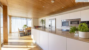 Moderne offene Küche mit weißen Hochglanzfronten, Holzdecke und Blick auf den Essbereich.