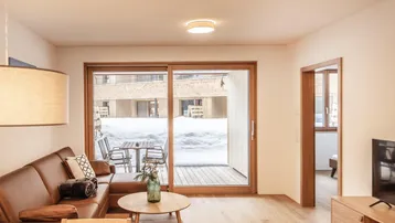 Helles Wohnzimmer mit bequemer Ledercouch, Holzboden und Zugang zur verschneiten Terrasse.