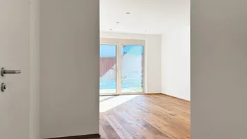 Helles Entrée mit Fliesenboden, das in einen lichtdurchfluteten Raum mit Holzboden und Gartenzugang führt.