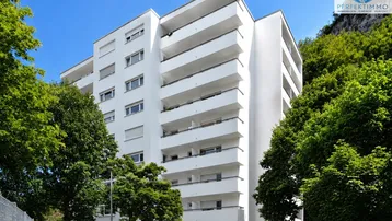Modernes Mehrfamilienhaus mit weißen Fassaden, vielen Balkonen und umgeben von grünen Bäumen.