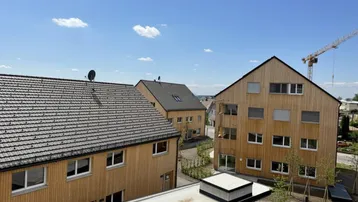 Neubauwohnungen mit Holzfassaden und Satteldächern in einer ländlichen Umgebung mit Baukran.