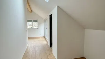 Heller Dachgeschossbereich mit Holzboden, Dachfenster und schrägen Wänden, ideal für individuelle Nutzung.