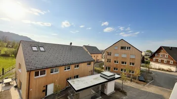 Moderne Wohngebäude mit Holzfassaden und Satteldächern in ländlicher Umgebung mit Bergblick.