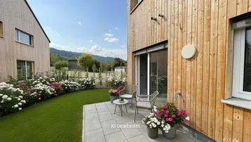 Gepflasterte Terrasse mit Gartenmöbeln, umgeben von Blumenbeeten und Rasenfläche mit Bergblick.