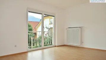 Helles Wohnzimmer mit hellem Holzboden, weißen Wänden und Zugang zu einem französischen Balkon mit Bergblick.