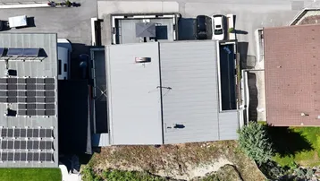Dachansicht eines Hauses mit Flachdach, Solaranlage und umliegender grüner Natur.