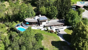 Luftaufnahme eines modernen Hauses mit Pool, umgeben von üppiger grüner Landschaft und Bäumen.