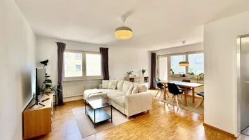 Helles Wohn- und Esszimmer mit Parkettboden, beiger Couch und Esstisch am Fenster.