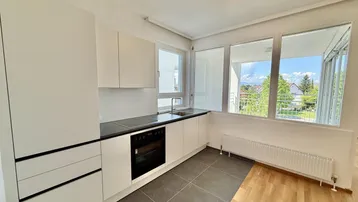 Moderne Küche mit weißen Schränken, dunkler Arbeitsplatte und Zugang zum Balkon.