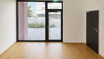 Heller Raum mit Holzboden und großen Fenstern, die einen Blick auf die Straße bieten.