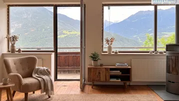Gemütliches Wohnzimmer mit Panoramablick auf die Berge, Holzboden und einem modernen Kaminofen.