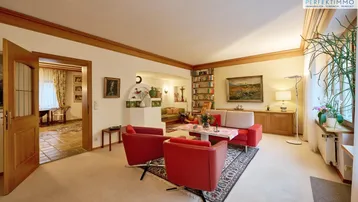 Gemütliches Wohnzimmer mit Teppichboden, roten Sesseln und traditionellem Kachelofen.